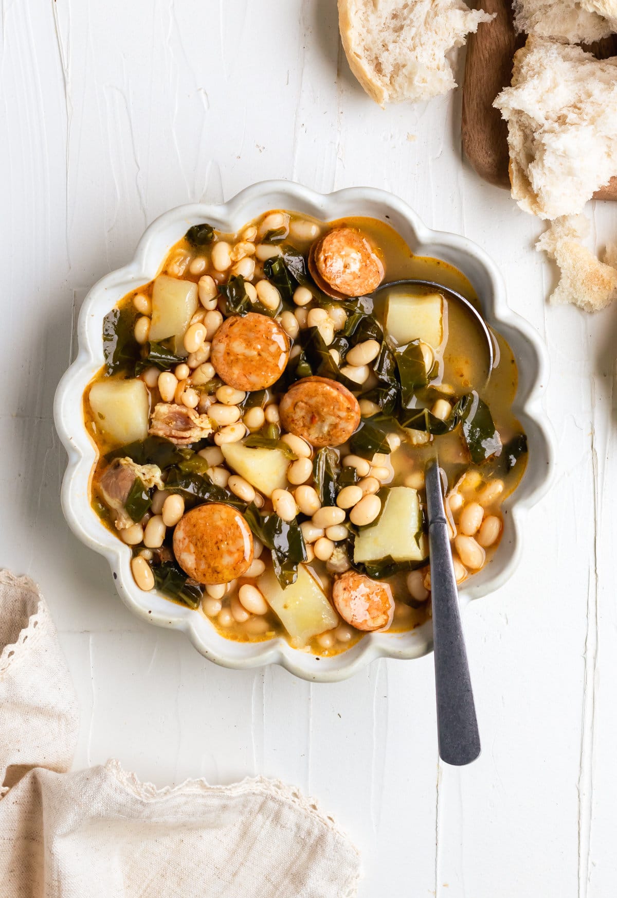 bowl of caldo gallego with chorizo, potatoes, greens, bacon in chicken broth with a side of crusty bread