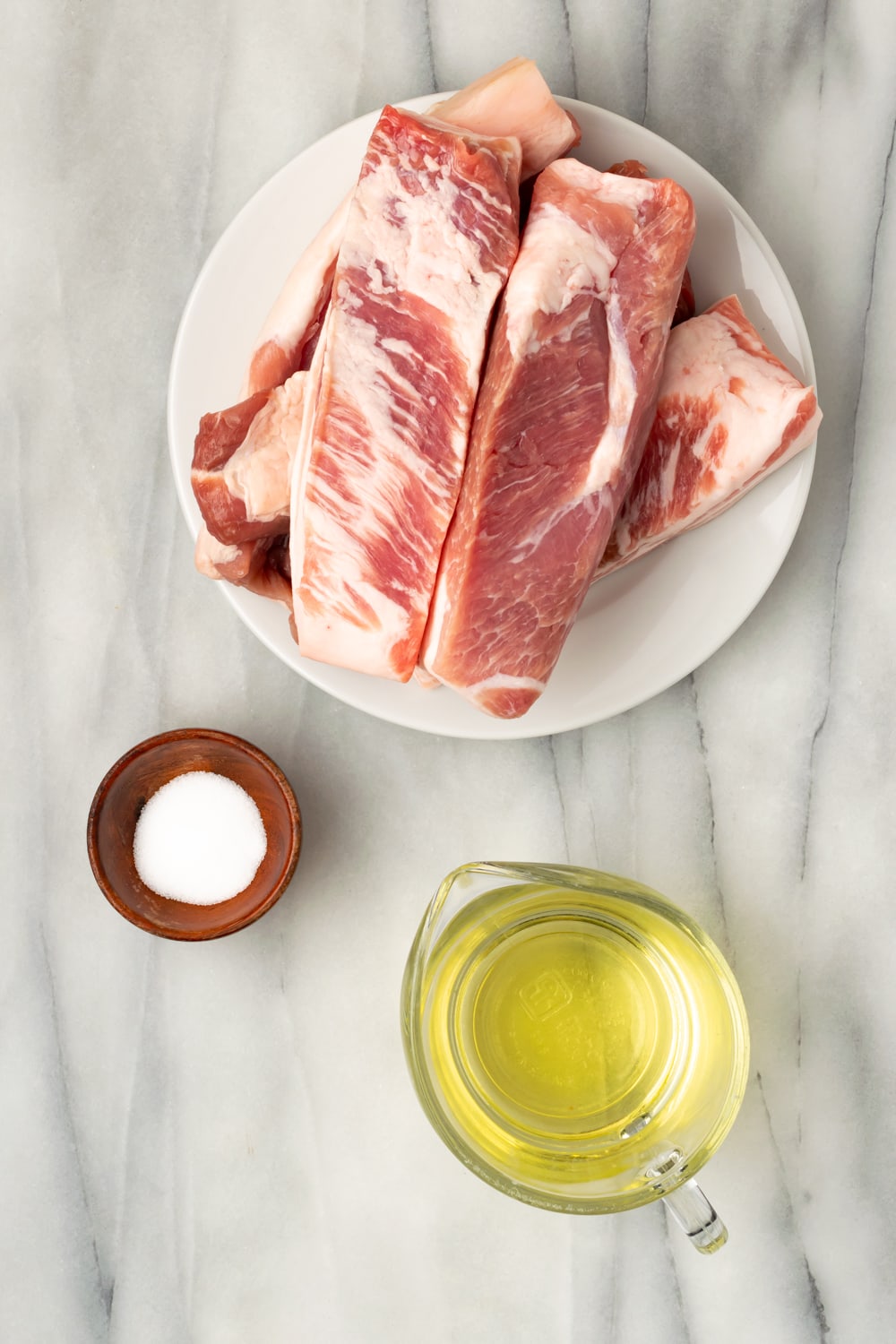 Ingredients for chicharrones de puerco on plates or bowls: pork belly, vegetable oil, salt.