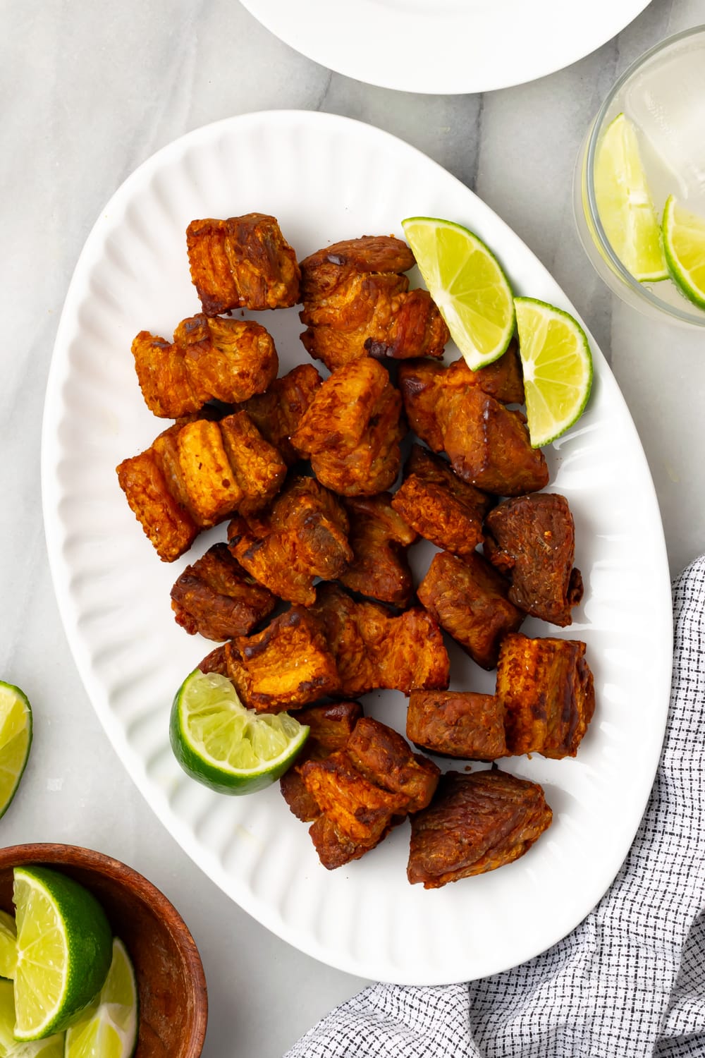 An overhead shot of chicharrones de puerco on a white platter with lime slices on the side on a white counter