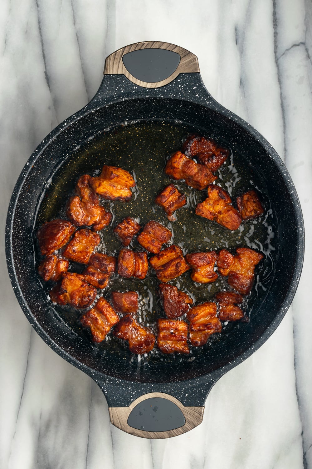 Pork belly pieces in a cast iron pan to make chicharrones de puerco on a marble countertop