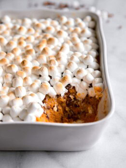 mashed sweet potato with toasted marshmallows on top in a casserole dish with a spoonful missing