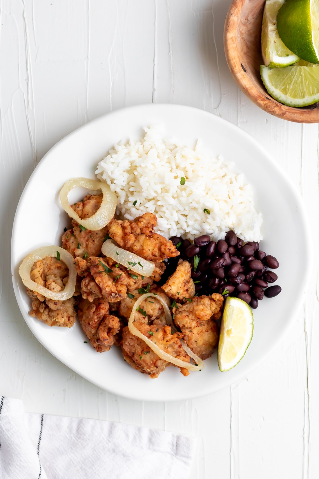 chicharron de pollo with sautéed onions, arroz con frijoles, and lime wedges