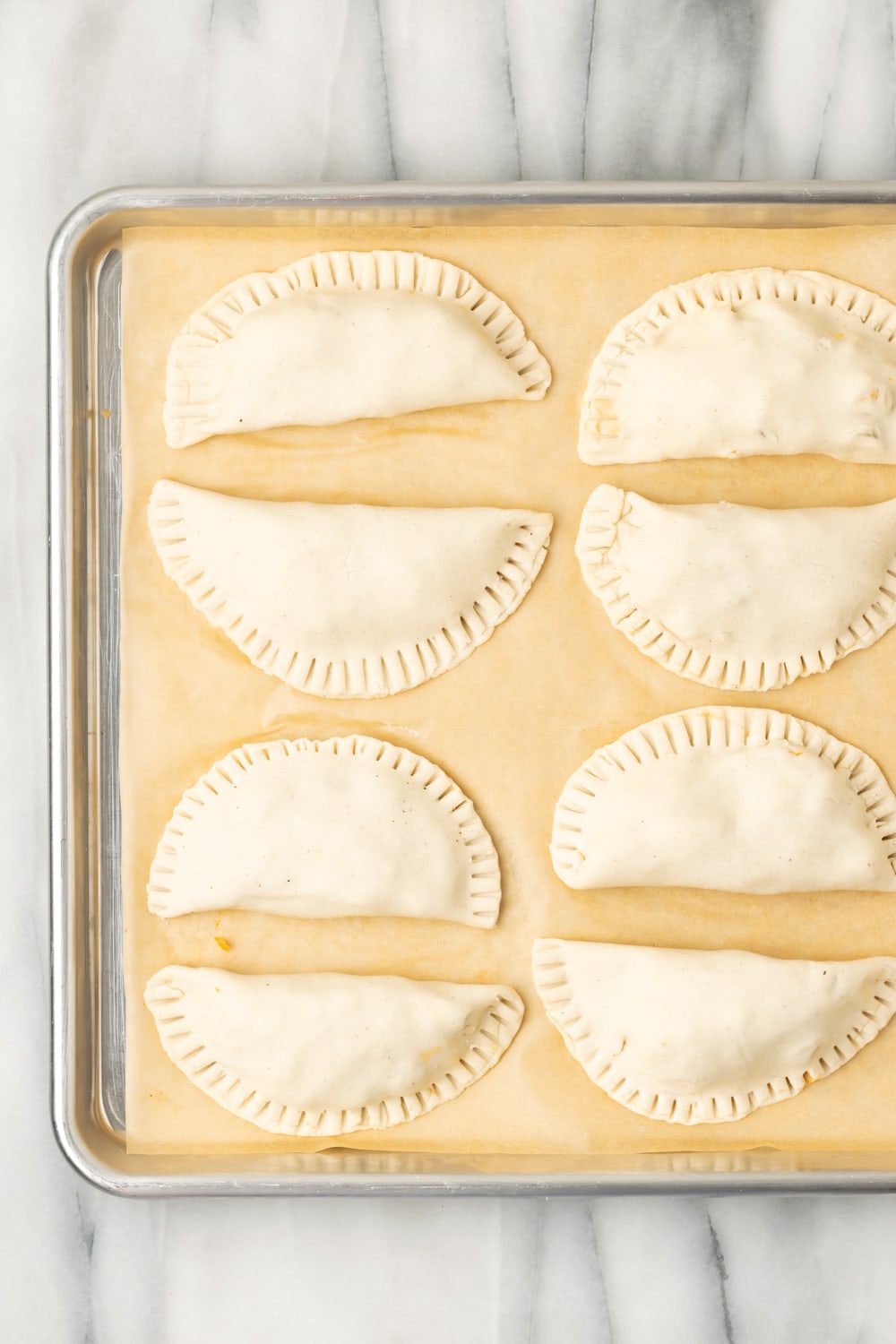 Cuban Chicken Empanadas that aren't fried yet on a parchment lined baking sheet
