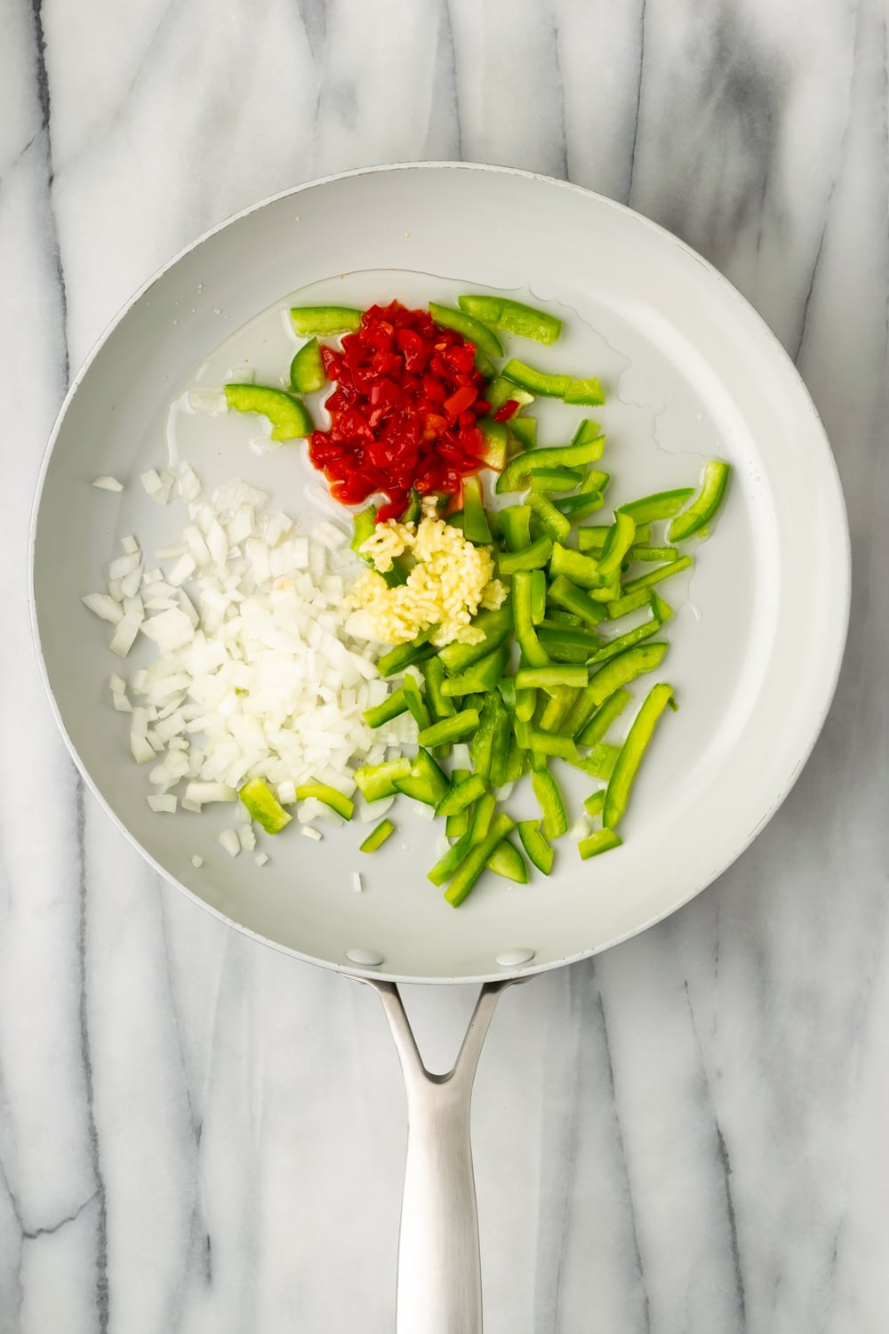 An overhead shot of a pan of onions, green peppers, garlic and pimentos to make sofrito for cuban chicken empanada filling