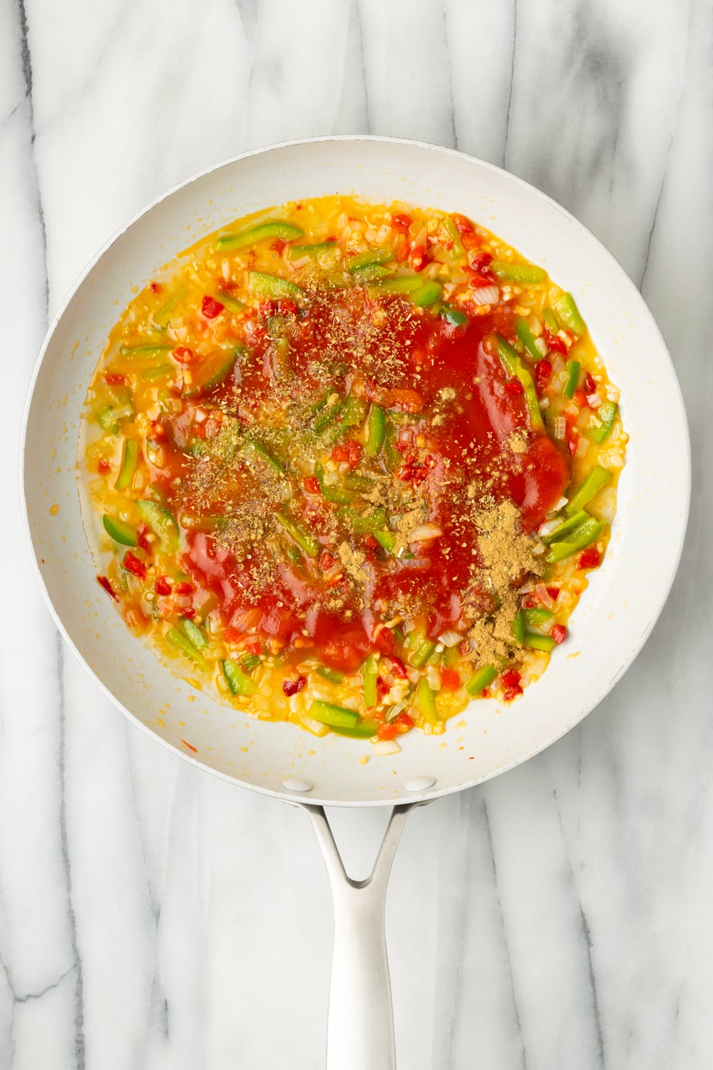 Tomato sauce, dry wine, and spices being added to a sofrito in a pan to make cuban chicken empanada filling on a marble background
