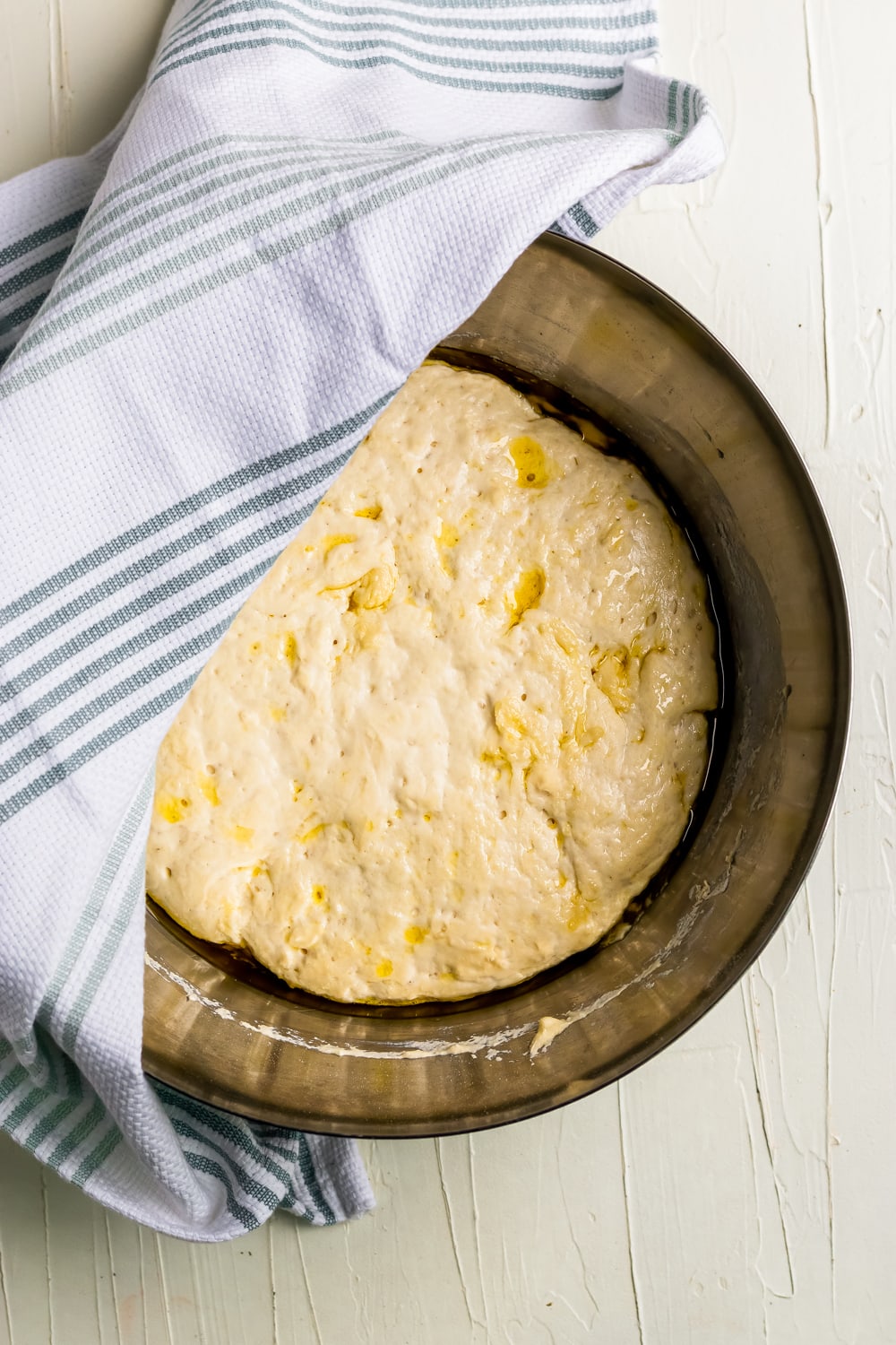 focaccia dough in the bowl with a towel waiting for it to rise