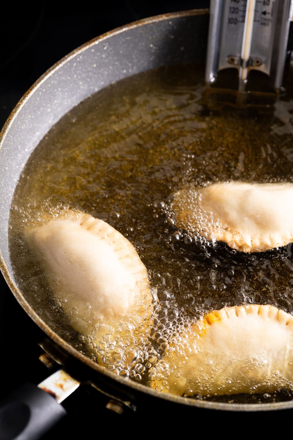 Three Guava Cheese empanadas in hot oil with a thermometer in the pot.