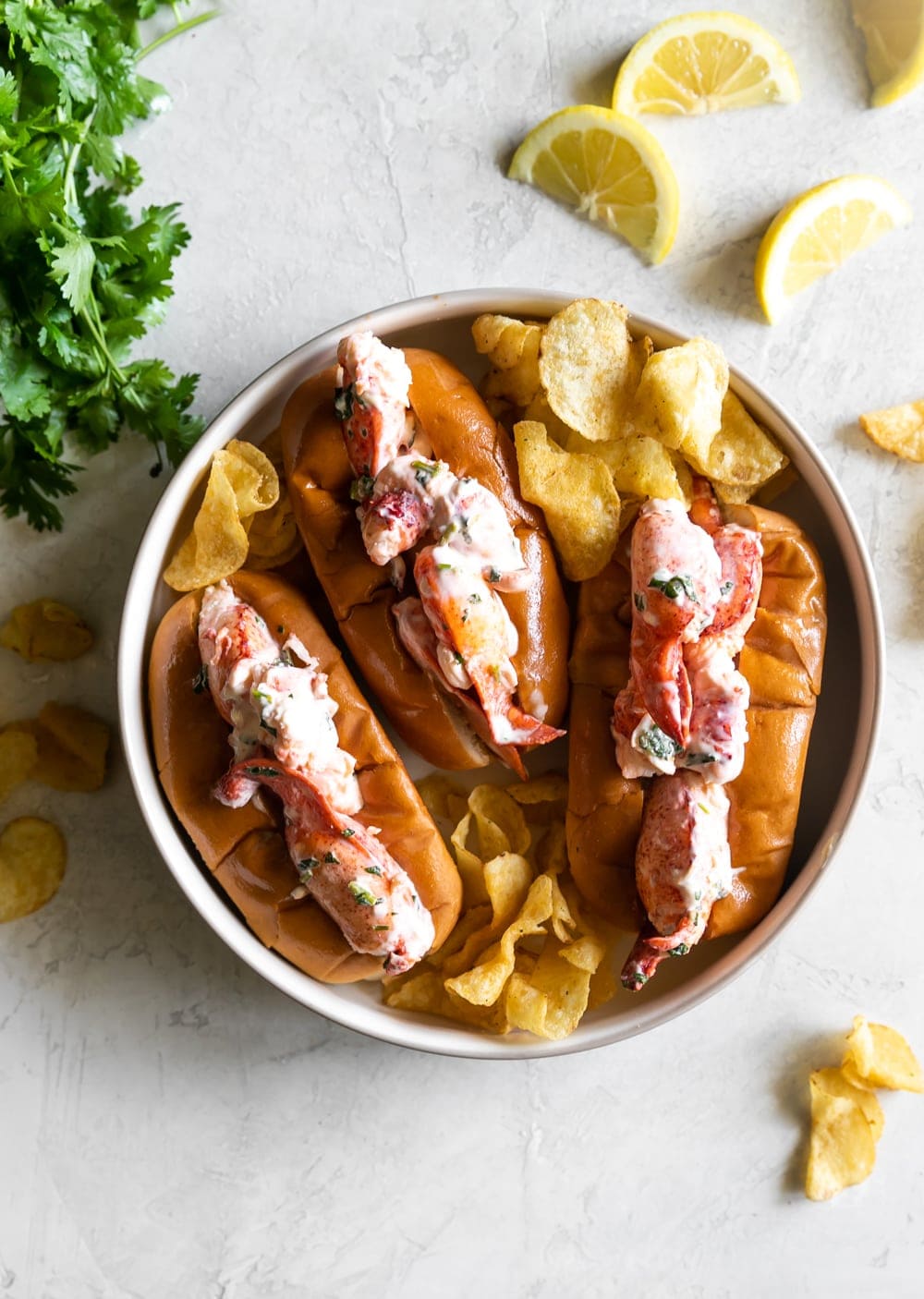 top view of maine lobster rolls with kettle cooked chips and lemon slices on buttered toasted buns