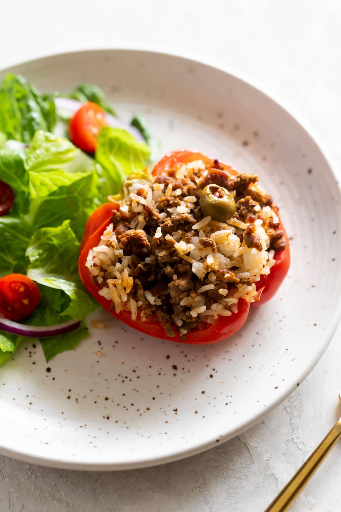picadillo stuffed pepper with a side salad on a speckled plate