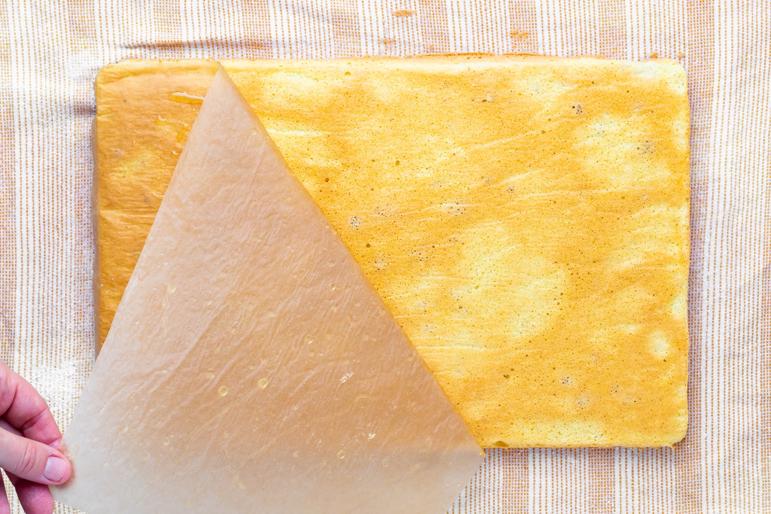 A guava swiss roll cake on a damp towel before being rolled up with the parchment paper being removed from the top.