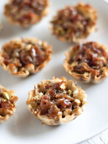 a plate with mini fillo shells filled with goat cheese, pistachios, bacon, honey, basil and garlic