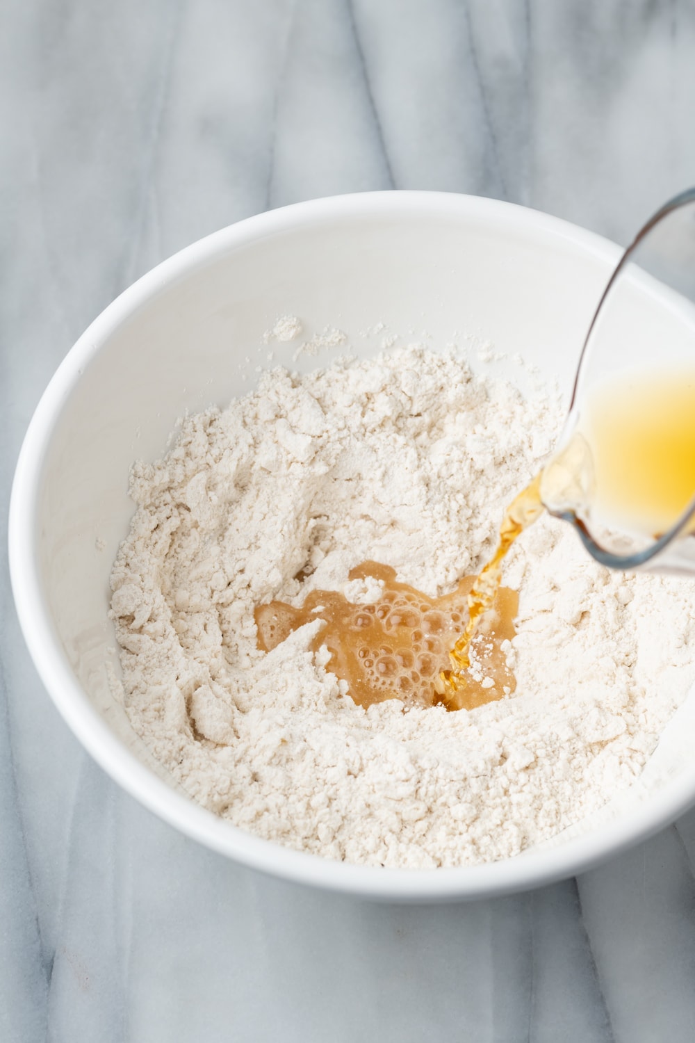 Cinnamon-sugar syrup being added to a white bowl with dry ingredients for empanada dough