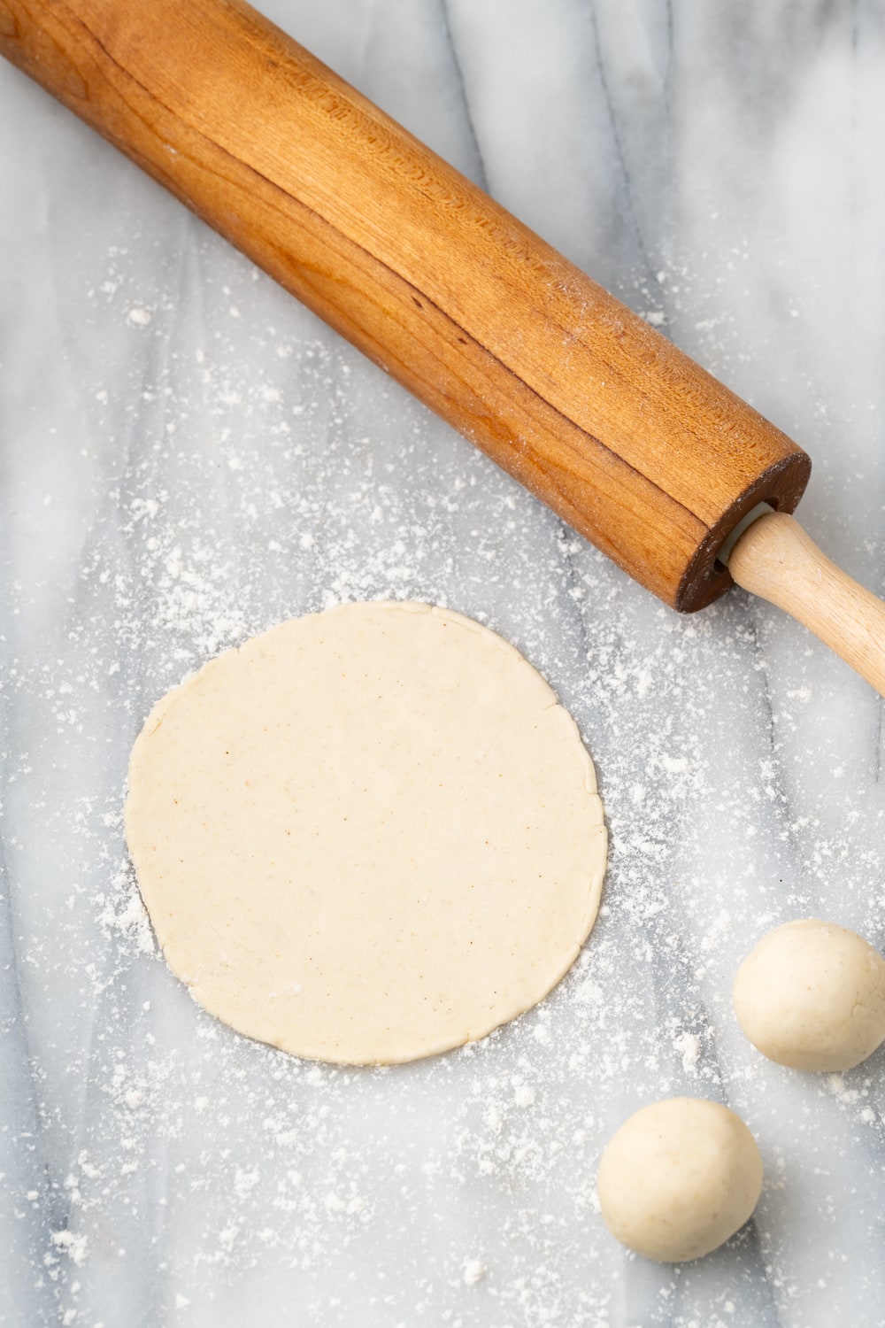 A photo showing how to make empanada dough into a round circle with a wooden rolling pin on the side