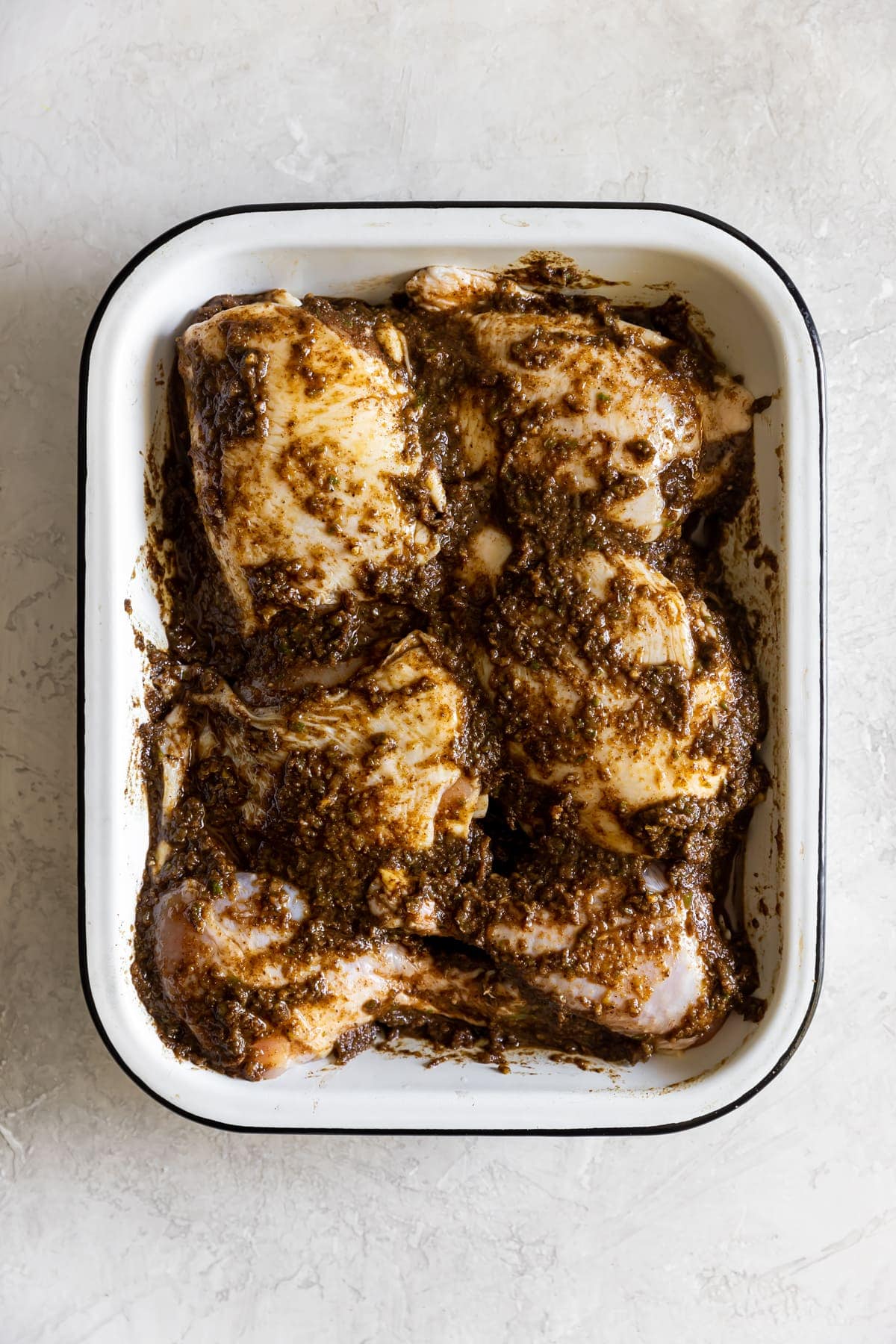 chicken being marinaded in jerk marinade in a baking dish before cooking