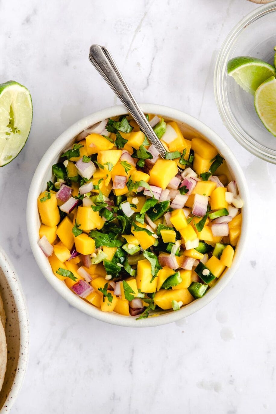bowl with mango salsa on a white table with cilantro and lime wedges