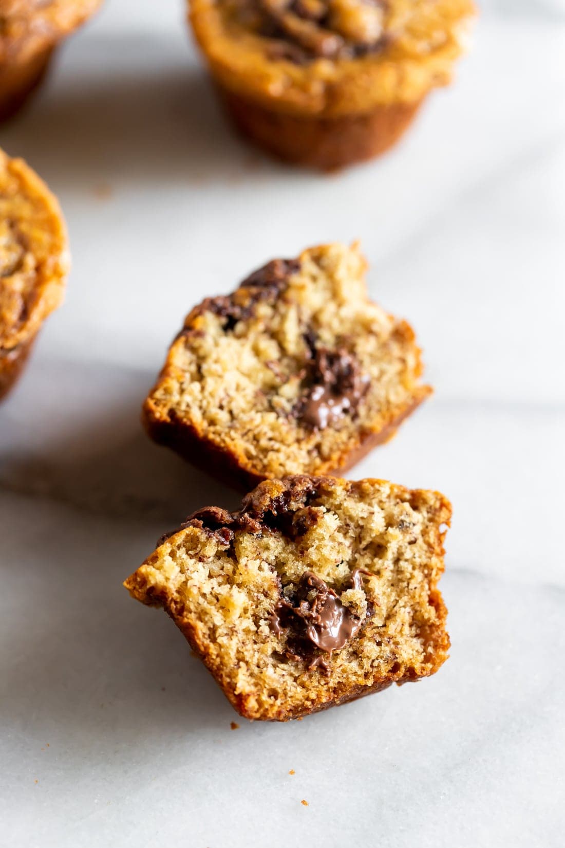 a nutella stuffed banana muffin sliced in half with hazelnut spread in the middle of the muffin on a marble slab